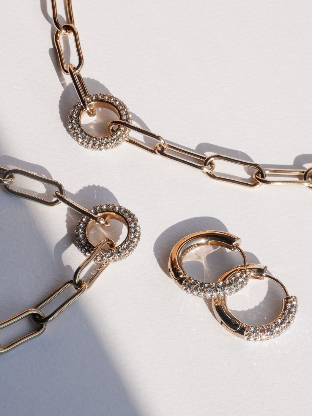 Tamaris Schmuck im Glitter-Donut-Design: goldfarbene Kette und Creolen mit funkelnden, rund gefassten Steinen, modern arrangiert auf hellem Hintergrund mit sanften Lichtreflexen.