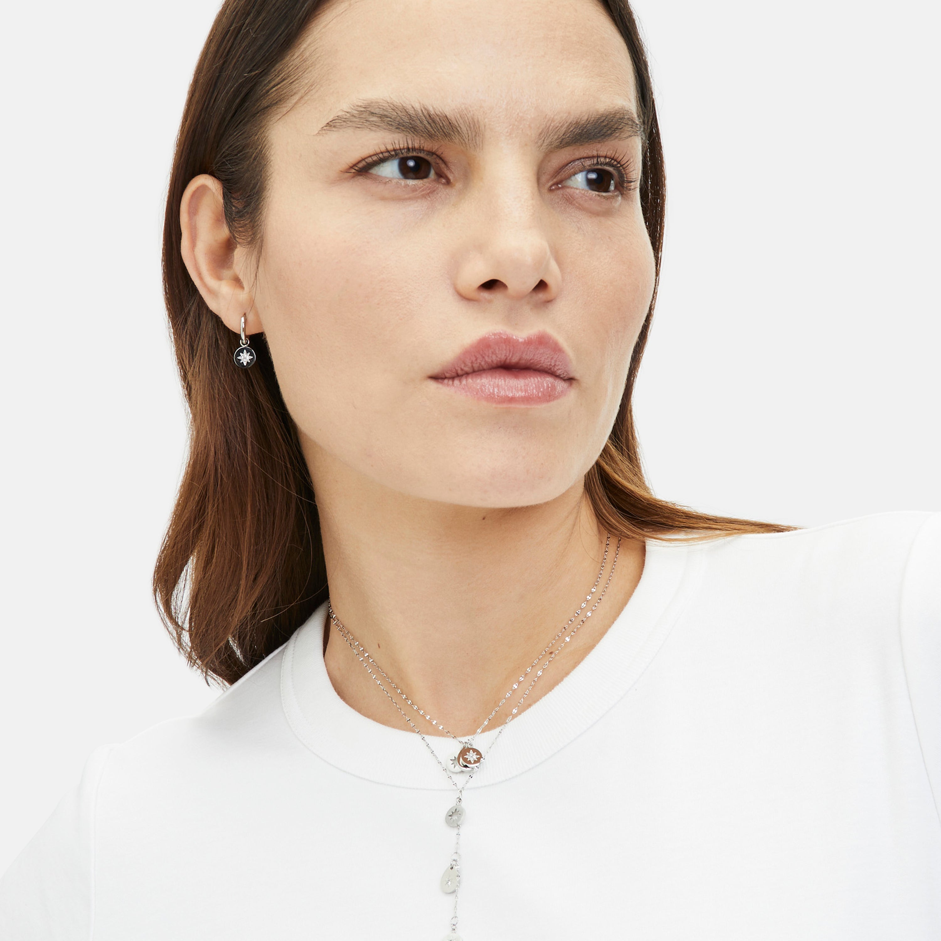 Frau im weißen Hemd trägt Tamaris Schmuck, darunter die Tamaris Halskette - The Sparkling Stars und passende Ohrringe.