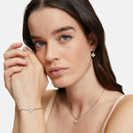 Eine Frau mit langen braunen Haaren trägt die Tamaris Creole - The Flower Pearl Halskette, Armband und Ohrringe mit passenden blumenförmigen Anhängern mit eleganten Glasperlen von Tamaris.