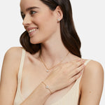 Eine Frau lächelt und trägt ein passendes goldenes Schmuckset mit Blumenmuster: Ohrringe, Armband und die Tamaris Halskette - The Flower Pearl von Tamaris, die ihrem Look Eleganz verleiht.