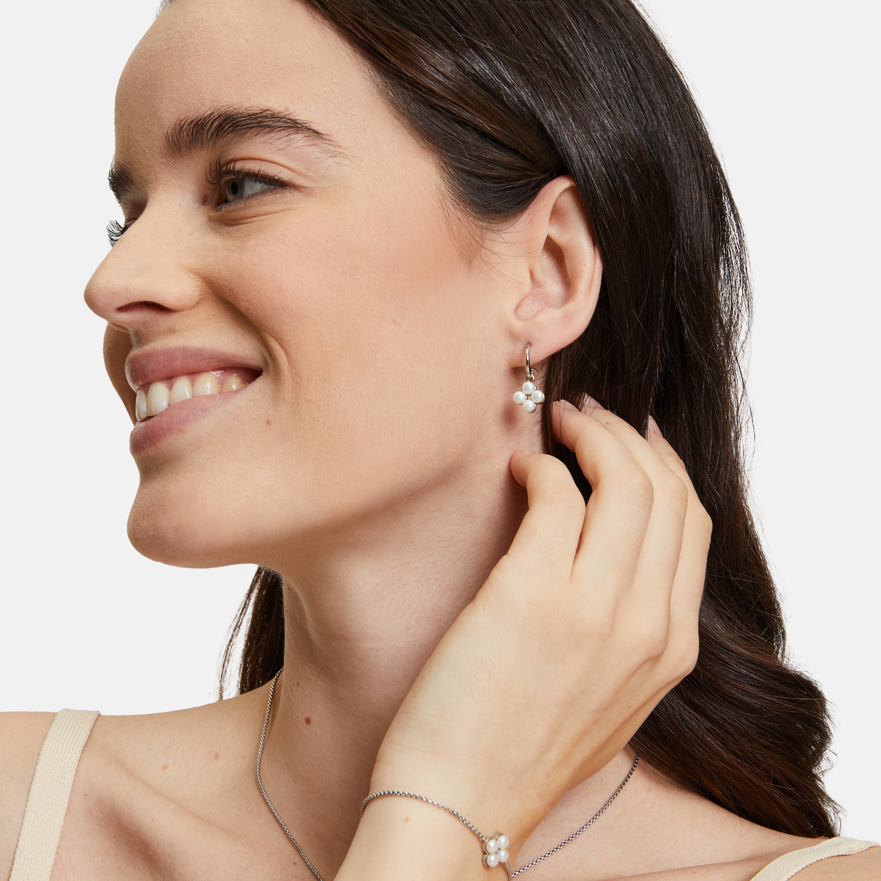 Eine Frau trägt Tamaris Creole - The Flower Pearl Ohrringe mit floralem Design und schimmernden Glasperlen von Tamaris.