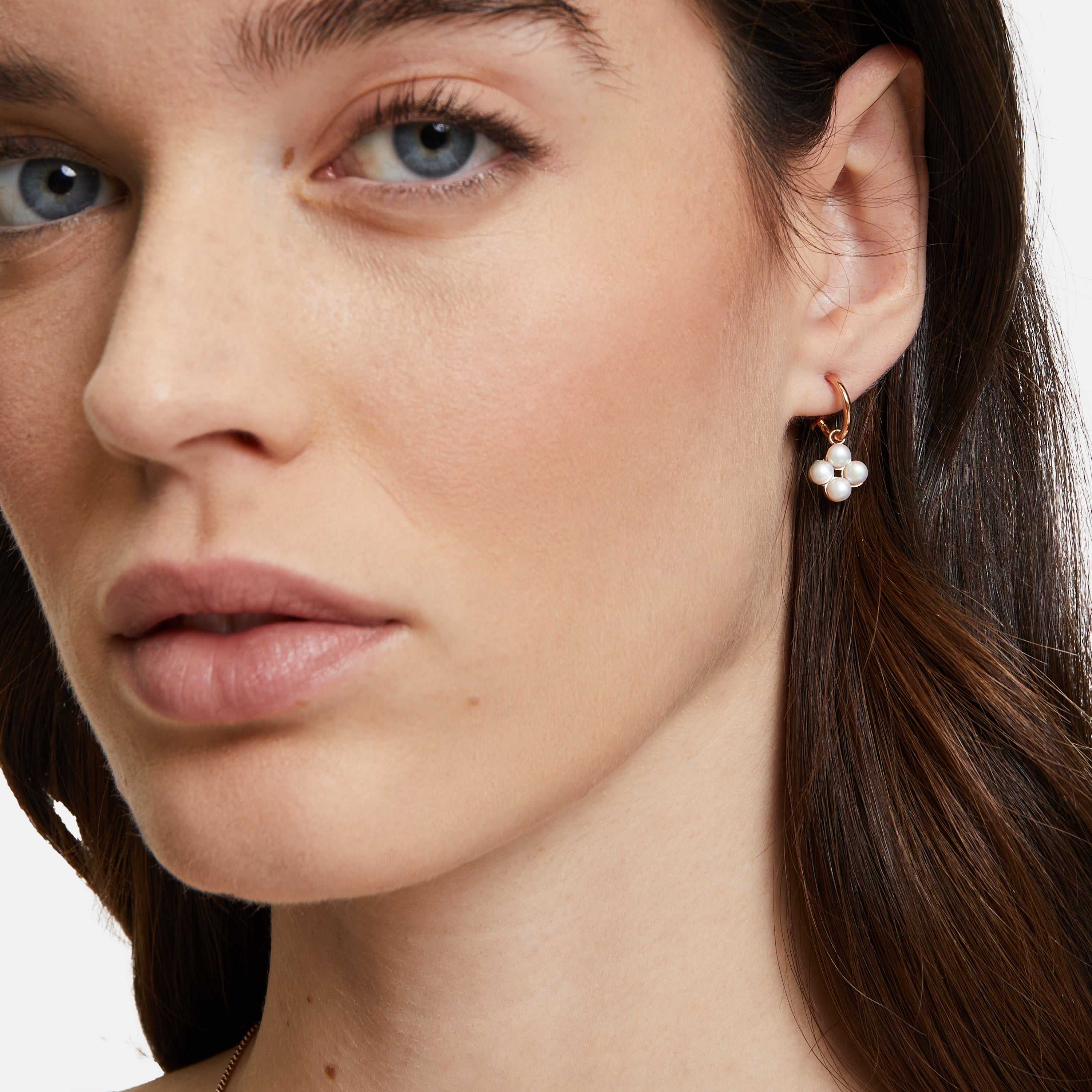 Nahaufnahme einer Frau mit braunen Haaren und natürlichem Make-up, die den Ohrring Tamaris Creole - The Flower Pearl von Tamaris mit floralem Muster trägt, gepaart mit einer dezenten Halskette.