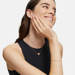 Eine lächelnde Frau trägt die Tamaris Halskette - The T-Pattern Heart mit passendem Armband und Ohrringen, die Hand sanft auf dem Gesicht - ein schönes Geschenk von Tamaris für einen besonderen Menschen.