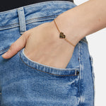 Eine Person trägt eine blaue Jeans und ein Tamaris Armband - The T-Pattern Heart von Tamaris, mit goldenen Herzdetails und einem Herzanhänger, eine Hand in der Tasche.