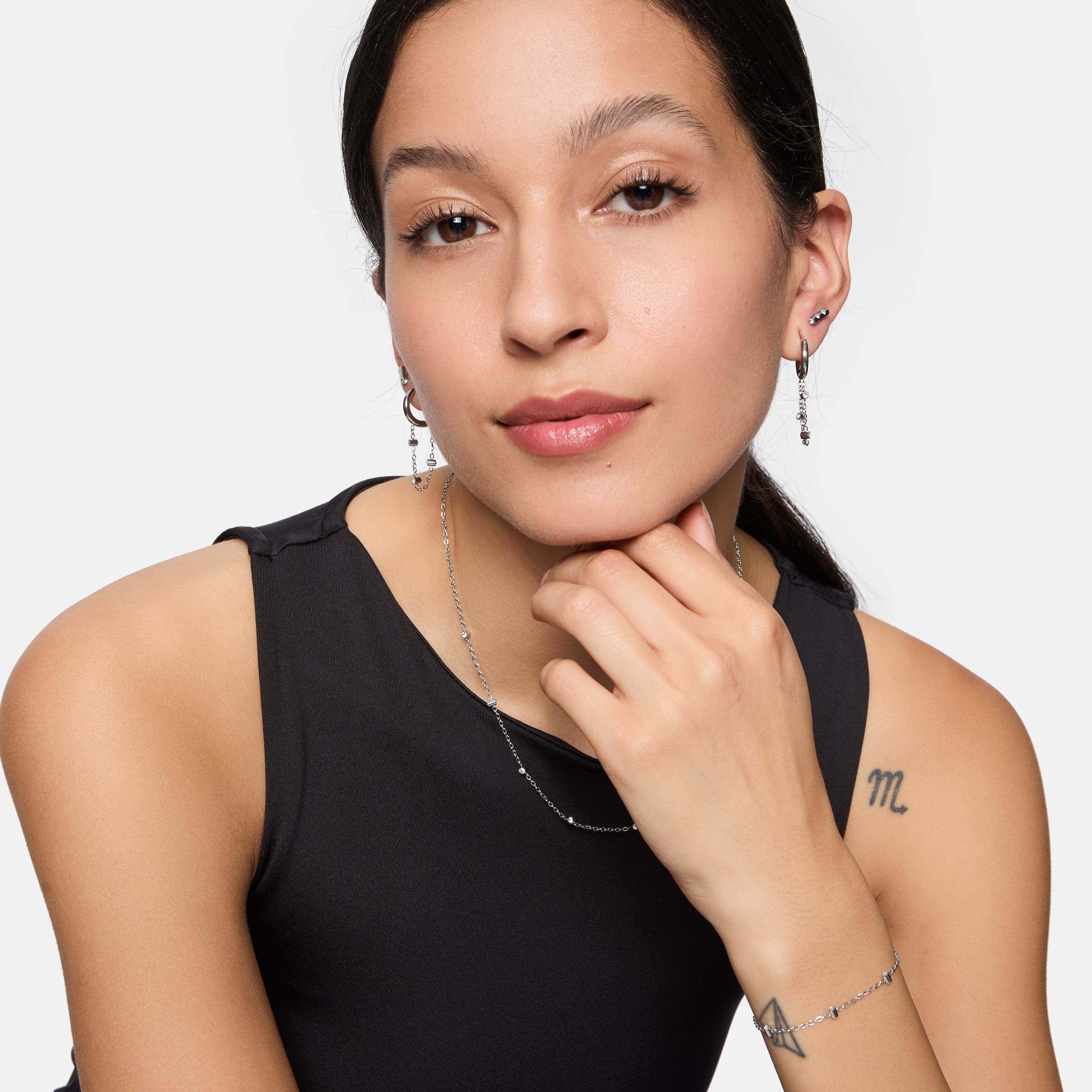 Eine Frau mit langen dunklen Haaren, einem ärmellosen schwarzen Oberteil und dezentem Make-up posiert selbstbewusst und trägt die Tamaris Halskette - Tiny Tubes von Tamaris als elegantes Accessoire.
