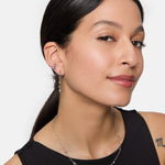 Frau mit langen dunklen Haaren trägt silberne Ohrringe, eine Tamaris Halskette - Tiny Tubes als elegantes Accessoire und ein ärmelloses schwarzes Oberteil.