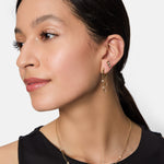 Frau mit langen dunklen Haaren trägt Tamaris Ohrstecker - Tiny Tubes und eine goldene Halskette, bekleidet mit einem ärmellosen schwarzen Top - ihr Tamaris-Schmuck glänzt mit eleganten Details.