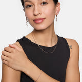 Eine Frau in einem schwarzen ärmellosen Top lächelt in die Kamera. Sie trägt eine passende Tamaris Halskette, ein Armband und Tamaris Tiny Tubes Ohrstecker mit funkelnden Glassteinen.