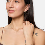 Eine Frau mit Tattoos auf Arm und Schulter trägt goldene Ohrringe in Herzform, ein Armband und die Tamaris Halskette - Graffiti Heart, die ihrem Accessoire Frauen-Look einen trendigen Touch verleiht.