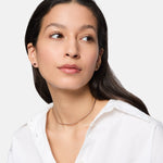 Frau mit langen dunklen Haaren, weißem Hemd und dünner Halskette, vervollständigt ihren Look mit Tamaris Ohrstecker - Modern Layering by Tamaris und verleiht ihm einen Hauch von Eleganz.