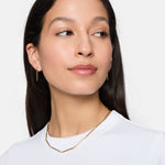 Frau mit langen dunklen Haaren, trägt Tamaris Creole - Modern Chain Ohrringe und ein weißes Oberteil, blickt leicht zur Seite.