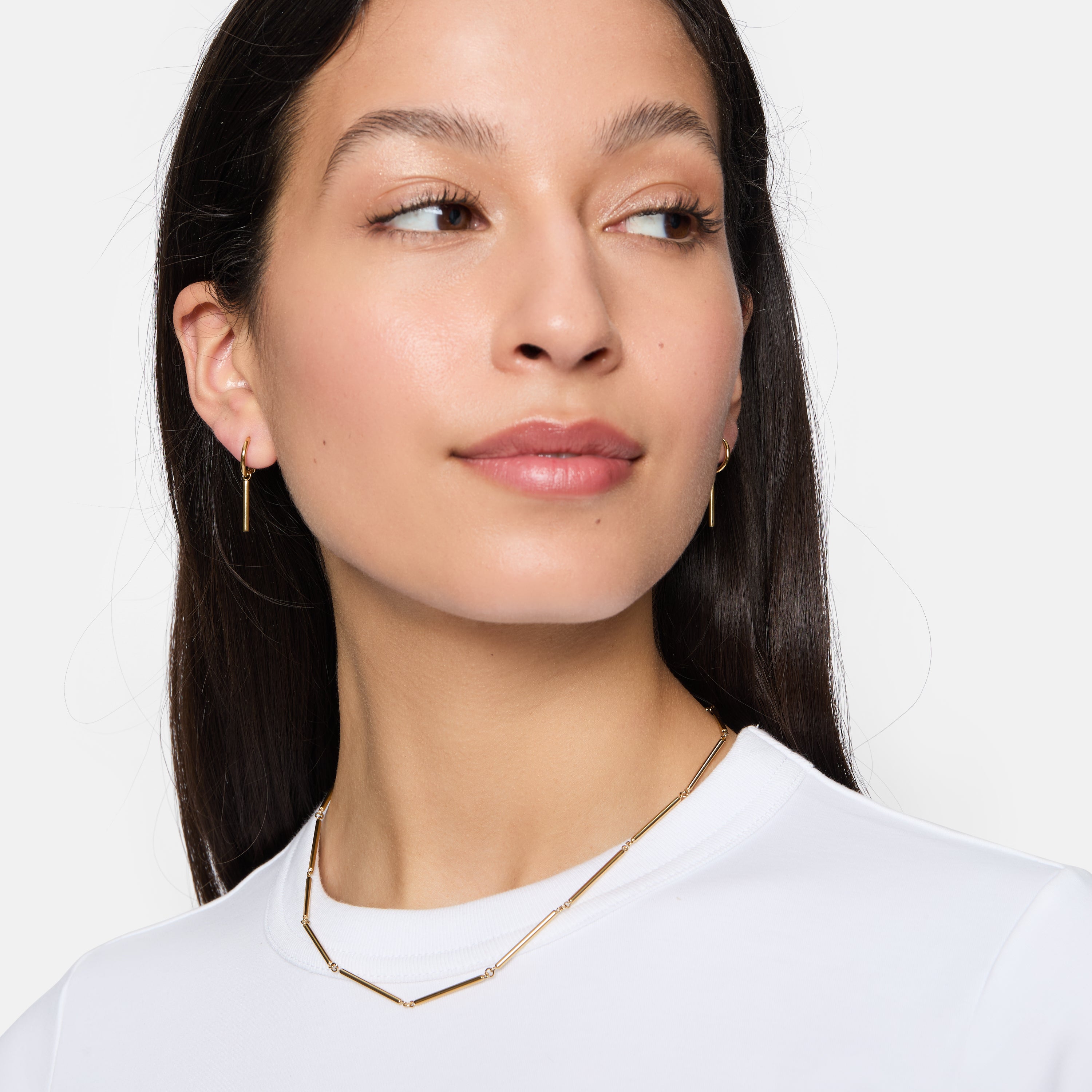 Frau mit langen dunklen Haaren, trägt Tamaris Creole - Modern Chain Ohrringe und ein weißes Oberteil, blickt leicht zur Seite.