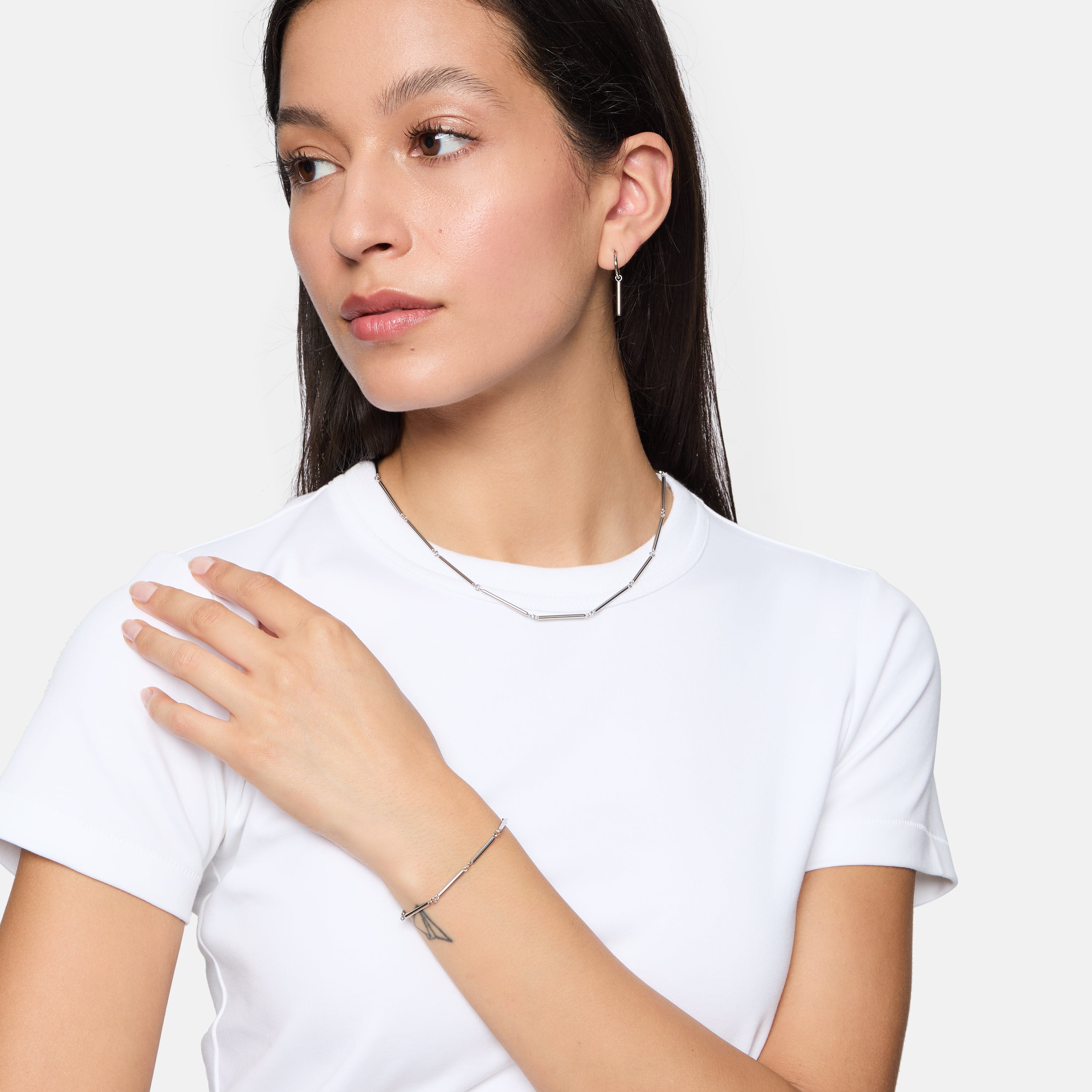 Frau im weißen T-Shirt trägt Tamaris Creole - Modern Chain Ohrringe und Silberschmuck und schaut mit der Hand auf der Schulter zur Seite.
