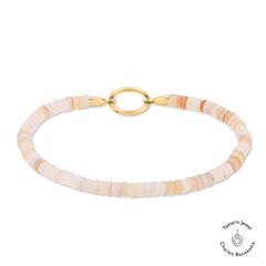 Das Tamaris Armband - All About Beads besteht aus hellpfirsich- und cremefarbenen Scheibenperlen, beigen Steinen, einem goldenen Verschluss und dem kultigen Tamaris Jewel Charms Logo.