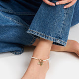 Nahaufnahme einer Person in Jeans, barfuß, die die Tamaris Fußkette - All About Beads by Tamaris mit einem Elefantenanhänger trägt.