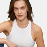 Eine Frau mit hellbraunem Haar trägt ein weißes Tank Top und das Tamaris Armband - All About Beads von Tamaris mit bunten Perlen, während sie vor einem schlichten Hintergrund sitzt.