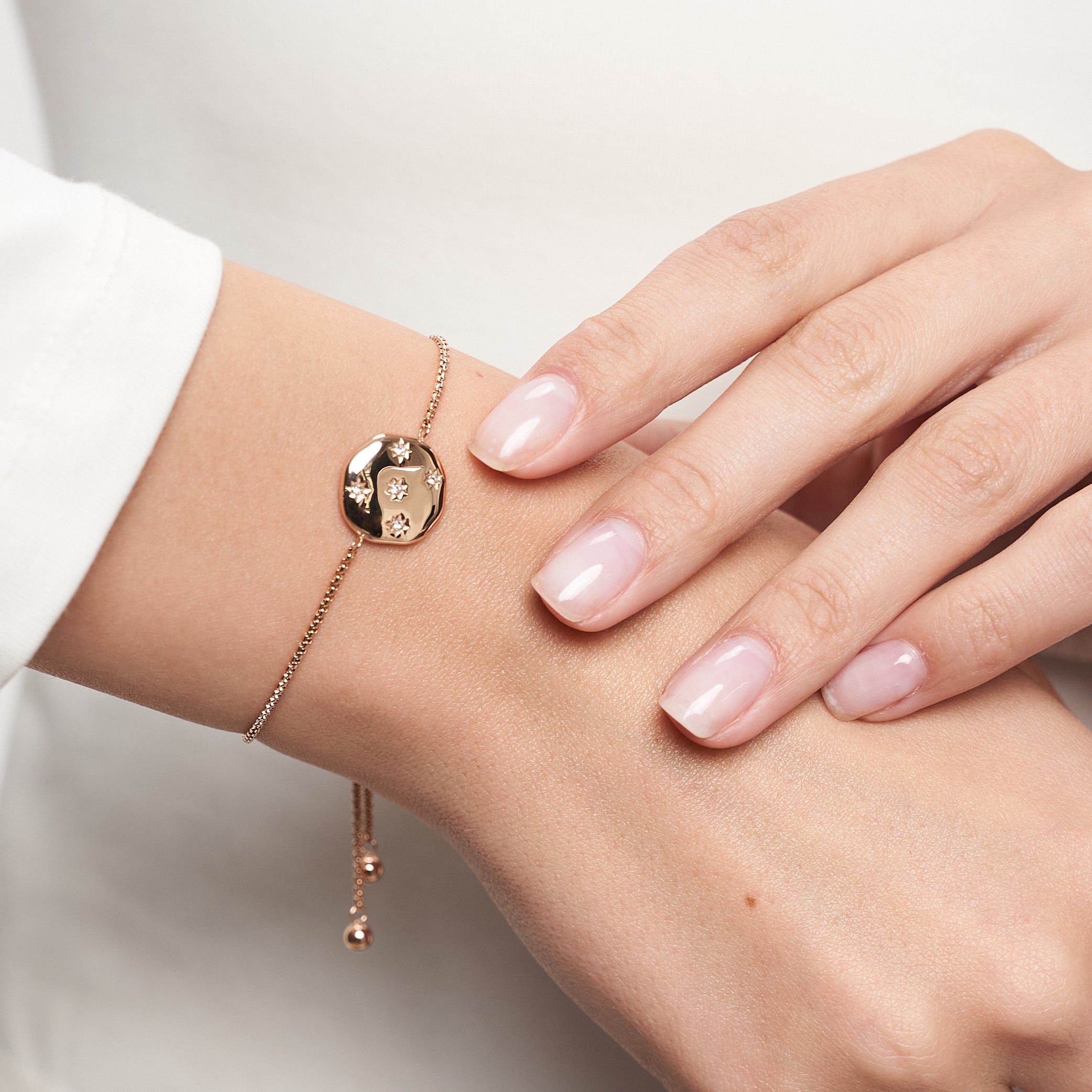 Nahaufnahme einer Frauenhand, die das Armband Tamaris - Little Twinkle von Tamaris trägt, das einen runden Anhänger mit funkelnden Zirkoniasteinen und hellrosa lackierten Nägeln aufweist.