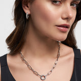 Eine elegant in Schwarz gekleidete Frau trägt die Tamaris Halskette - Glitter Donuts und dazu passende Creolen, alles von Tamaris in modernem Design.