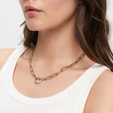Frau trägt eine Tamaris Halskette - Glitter Donuts - Goldkette von Tamaris mit rundem Anhänger - elegant gestylt mit einem weißen Tanktop.