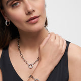 Frau mit eleganten Accessoires: silberne Hoop-Ohrringe, Zirkonia-Anhänger und das Tamaris Armband "Glitter Donuts" - alles stilvoll zum schwarzen Top kombiniert.