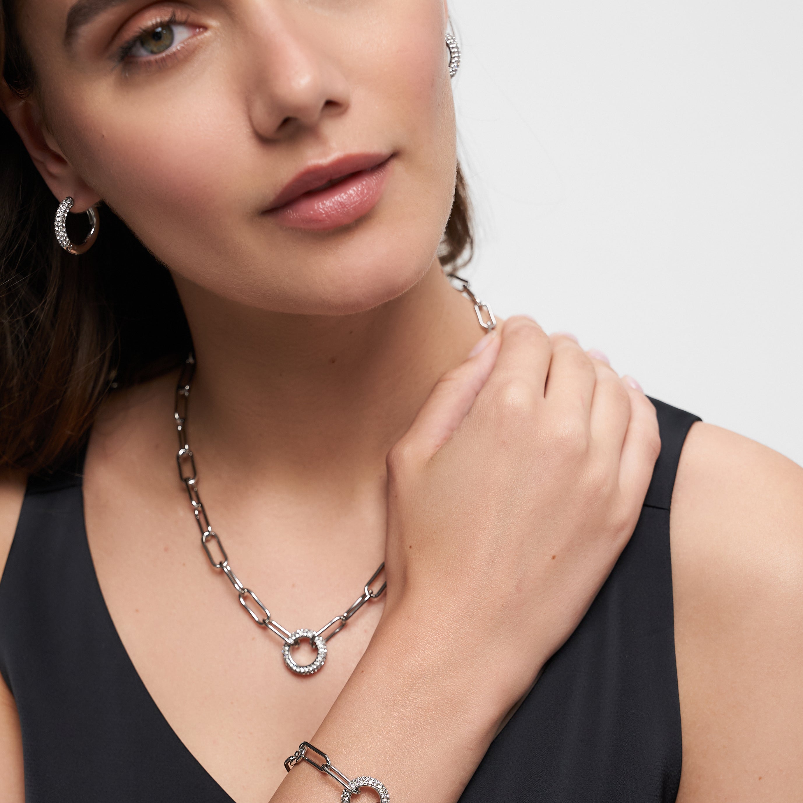 Frau mit eleganten Accessoires: silberne Hoop-Ohrringe, Zirkonia-Anhänger und das Tamaris Armband "Glitter Donuts" - alles stilvoll zum schwarzen Top kombiniert.