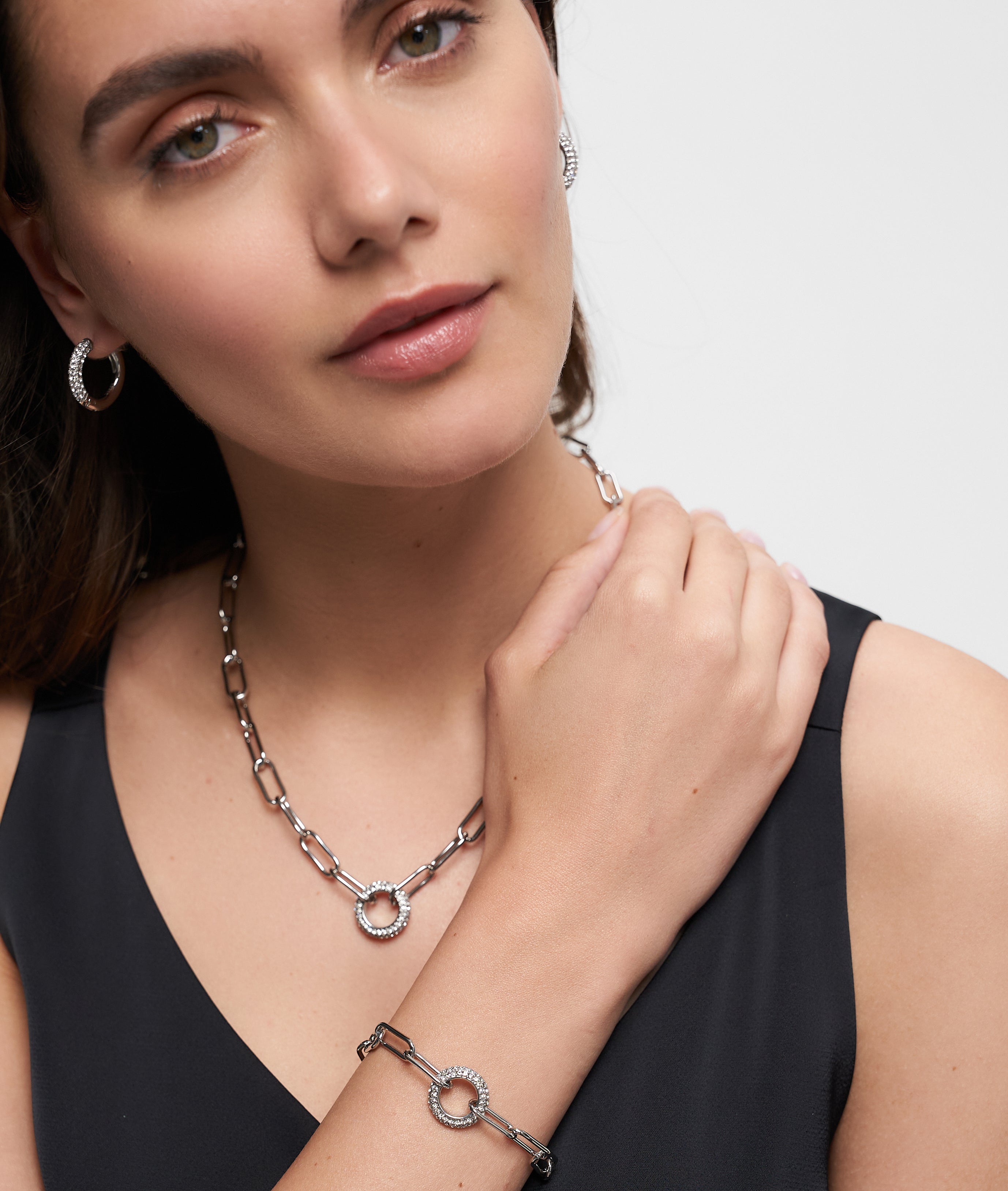 Frau mit eleganten Accessoires: silberne Hoop-Ohrringe, Zirkonia-Anhänger und das Tamaris Armband "Glitter Donuts" - alles stilvoll zum schwarzen Top kombiniert.