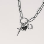 Die Tamaris Halskette - Charm Series: Eine elegante Silberkette mit Kreuz-, Herz- und Hufeisenanhängern der Marke Tamaris auf weißem Hintergrund.