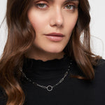Frau mit gewelltem braunem Haar trägt ein schwarzes Oberteil und eine Tamaris Halskette - Charm Series by Tamaris - eine silberne Kette mit einem runden Anhänger.