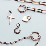 Tamaris Halskette - Charm Series: Goldketten mit Kreuz-, Herz-, Hufeisen- und runden Anhängern von Tamaris, die auf einer weißen Oberfläche für einen eleganten Look sorgen.