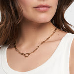 Eine Frau trägt die Tamaris Halskette - Charm Series, eine goldene Halskette mit ovalen Gliedern und rundem Verschluss von Tamaris, zu einem weißen Tanktop.