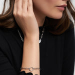 Eine Frau in einem schwarzen Oberteil berührt ihr Gesicht, während sie eine silberne Gliederkette und das Tamaris Armband aus der Charm Series von Tamaris trägt, das eleganten Damen Schmuck wunderschön zur Geltung bringt.