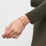 Eine mit dem Tamaris Armband - Charm Series by Tamaris geschmückte Hand vor einem olivgrünen Langarm-Top - der ideale Schmuck für Frauen.