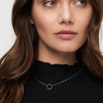Frau mit langen braunen Haaren trägt ein schwarzes Oberteil und die Tamaris Halskette aus der Charm Series - eine schlichte Silberkette mit einem runden Anhänger, perfekt für Fans von elegantem Schmuck von Tamaris.