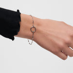 Eine Hand, die das Tamaris Armband - Charm Series mit einem runden Anhänger vor einem schlichten Hintergrund trägt - ein perfektes Beispiel für eleganten Damenschmuck von Tamaris.