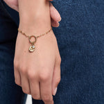 Eine Hand zeigt das Tamaris Armband - Charm Series, ein goldenes Kettenarmband mit Herz- und Rundanhängern von Tamaris, das auf blauem Denim einen perfekten Akzent für eleganten Damenschmuck setzt.