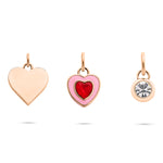 Das Tamaris Charms Bundle - Charm Series von Tamaris enthält drei goldene Charms: ein schlichtes Herz, ein rosafarbenes Herz mit rotem Edelstein und einen runden Zirkonia-Anhänger für funkelnde Eleganz.