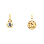 Tamaris Charms Bundle - Charm Serie: Zwei goldene Tamaris-Charms - einer mit funkelnden Zirkonia, der andere mit eingraviertem Engelcharm - verleihen dem weißen Hintergrund einen Hauch von Eleganz.