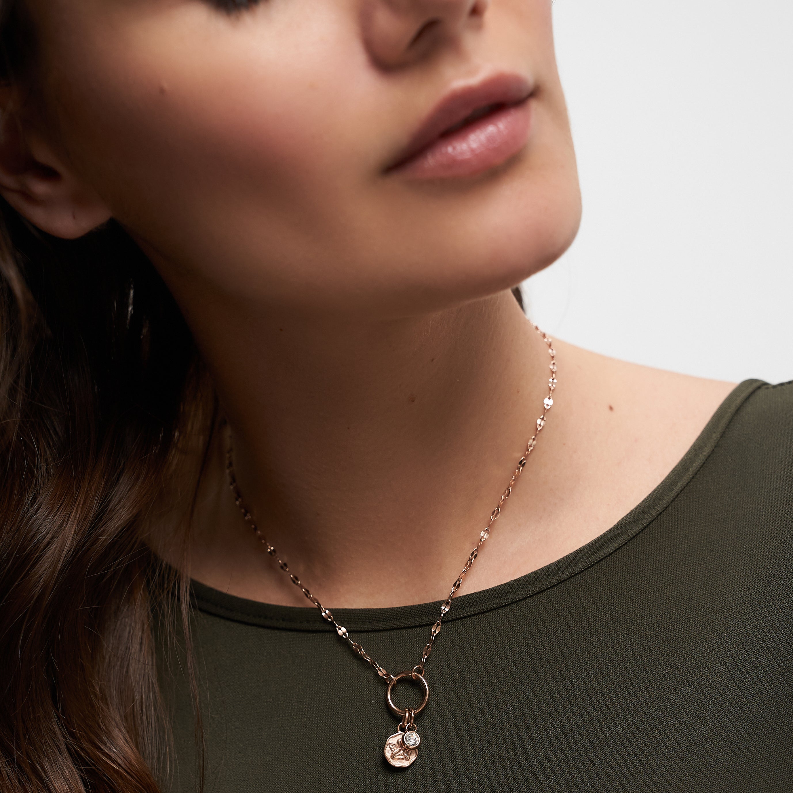 Frau trägt eine Tamaris Charms Bundle-Halskette aus der Charm-Serie mit einem runden Anhänger, kombiniert mit einem olivgrünen Oberteil.