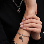 Eine Frau trägt das Tamaris Charms Bundle - Charm Series Silberkettenarmband mit Herz- und Schwertanhängern, gepaart mit einer passenden Tamaris-Halskette.