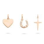 Das Tamaris Charms Bundle - Charm Series von Tamaris besteht aus drei roségoldenen Anhängern - einem Herz, einem mit Juwelen besetzten Hufeisen und einem einfachen Kreuz - perfekter Schmuck für Frauen auf weißem Hintergrund.