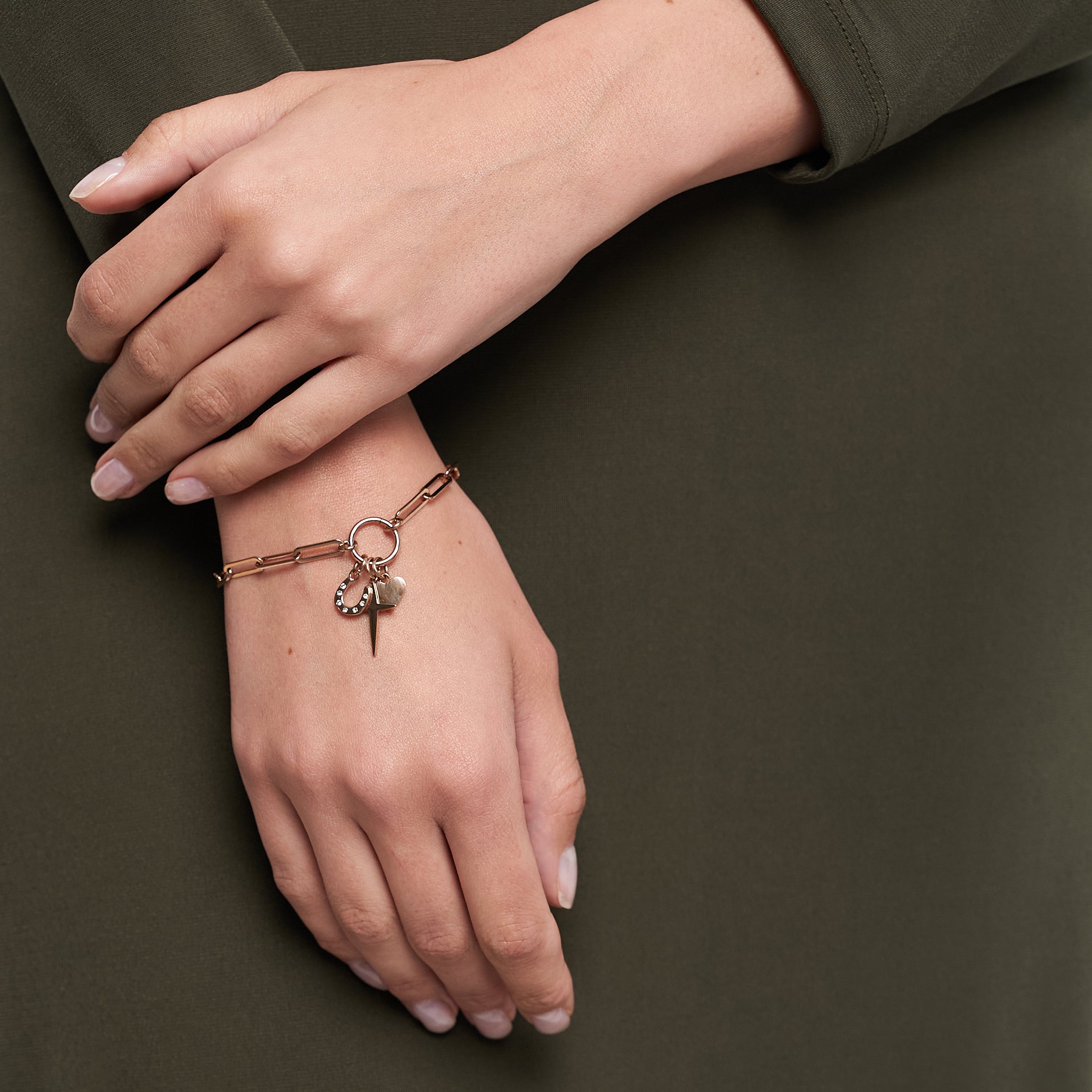 Eine Hand trägt das Tamaris Charms Bundle - Charm Series Goldarmband mit rundem Charm und Spike zu einem olivgrünen Kleid - eleganter Tamaris-Schmuck für jeden Anlass.