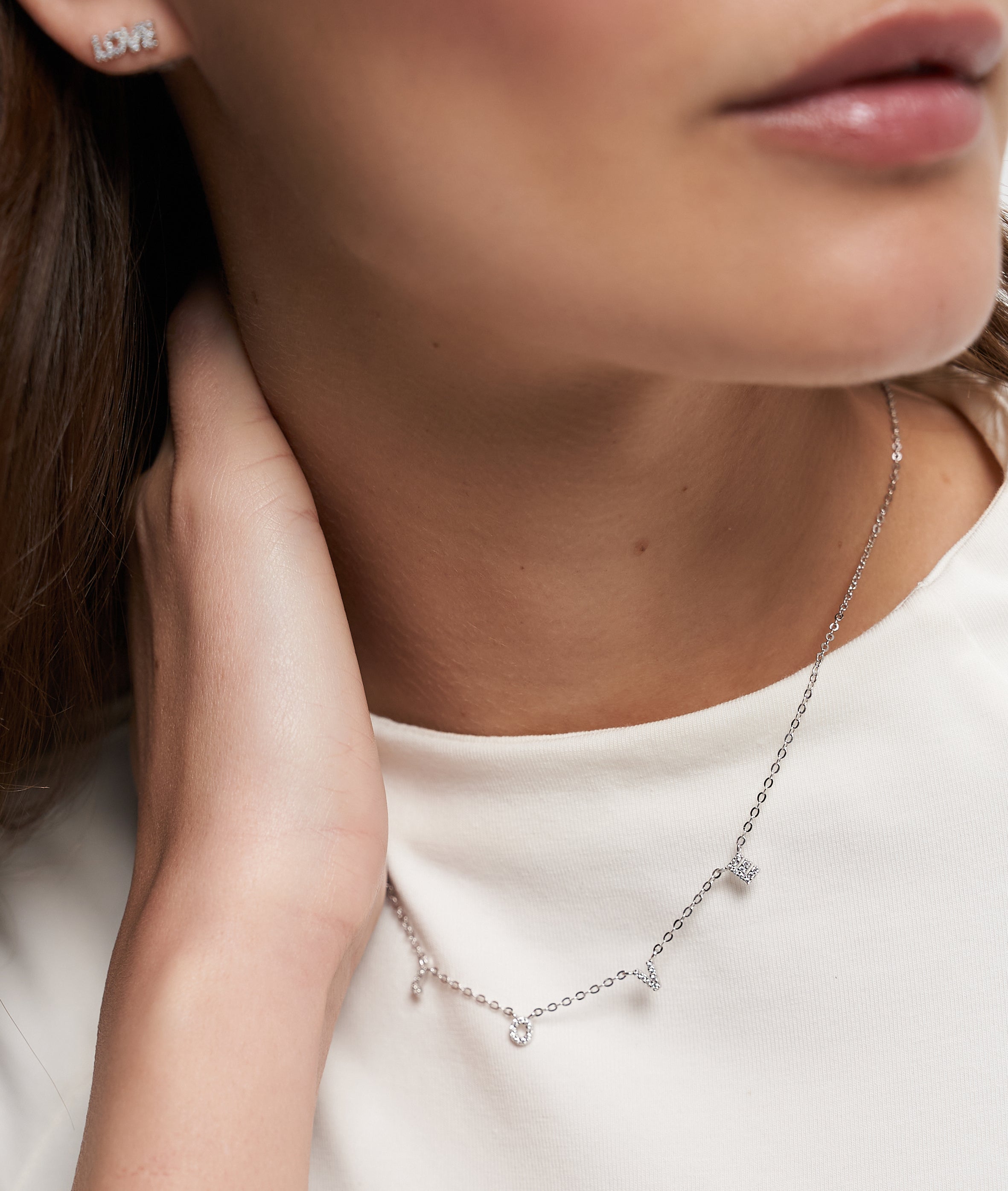 Nahaufnahme einer Frau, die die Tamaris Halskette aus der Silver Love Collection mit Zirkoniasteinen, LOVE-Anhängern und einem passenden LOVE-Ohrring von Tamaris trägt.