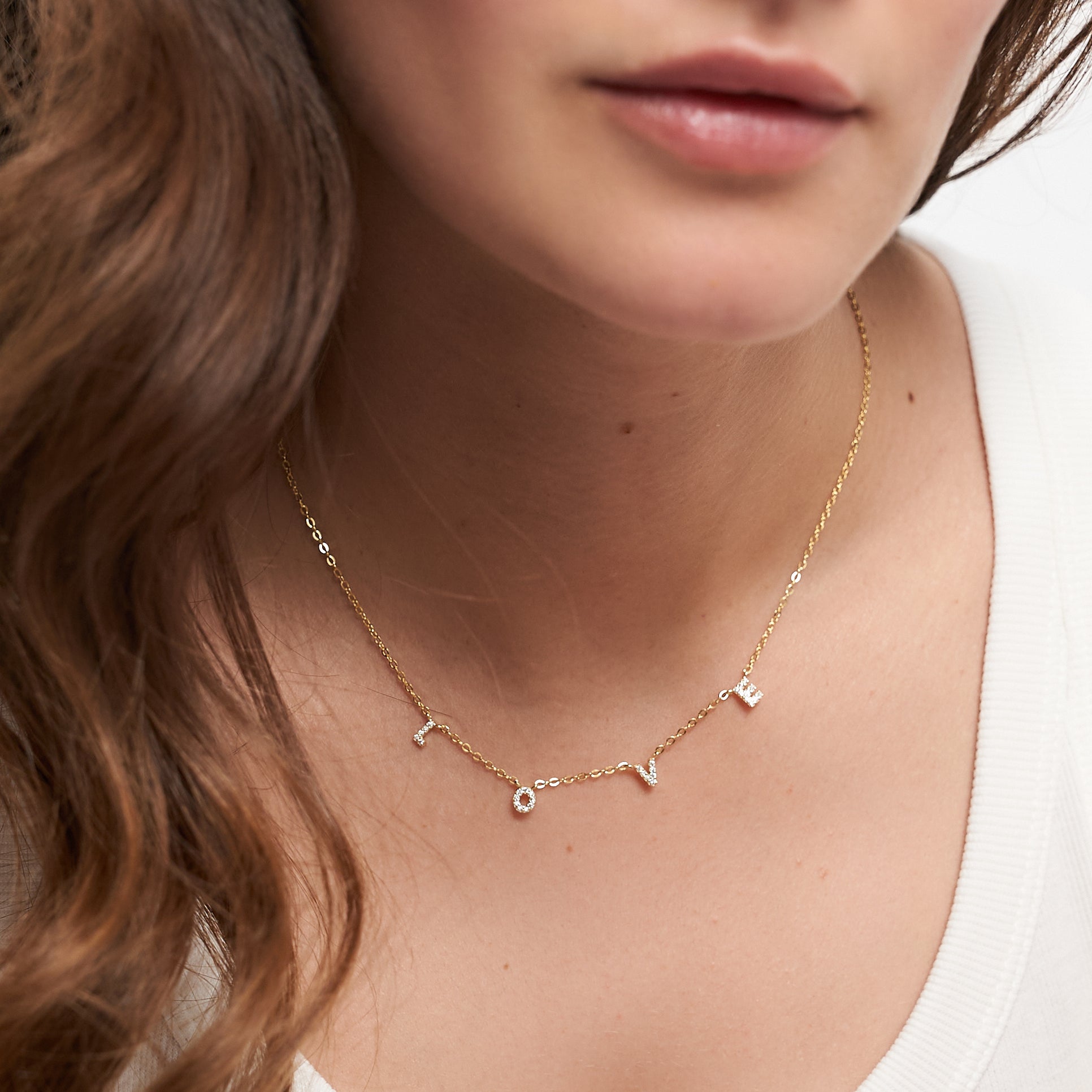 Eine Frau trägt die Tamaris Halskette aus der Silver Love Collection mit LOVE Anhänger und funkelnden Zirkoniasteinen, kombiniert mit einem schlichten weißen Top.