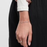 Eine Hand, die das Tamaris Armband aus der Silver Love Collection von Tamaris mit Zirkoniasteinen und einem Silberring trägt, ruht auf einer schwarzen Hose.