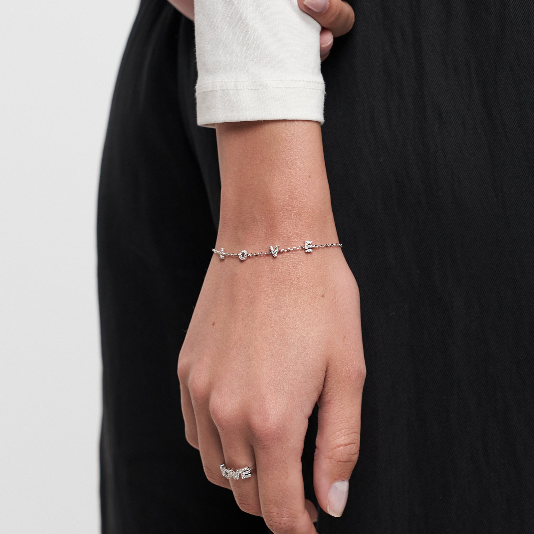 Eine Hand, die das Tamaris Armband aus der Silver Love Collection von Tamaris mit Zirkoniasteinen und einem Silberring trägt, ruht auf einer schwarzen Hose.