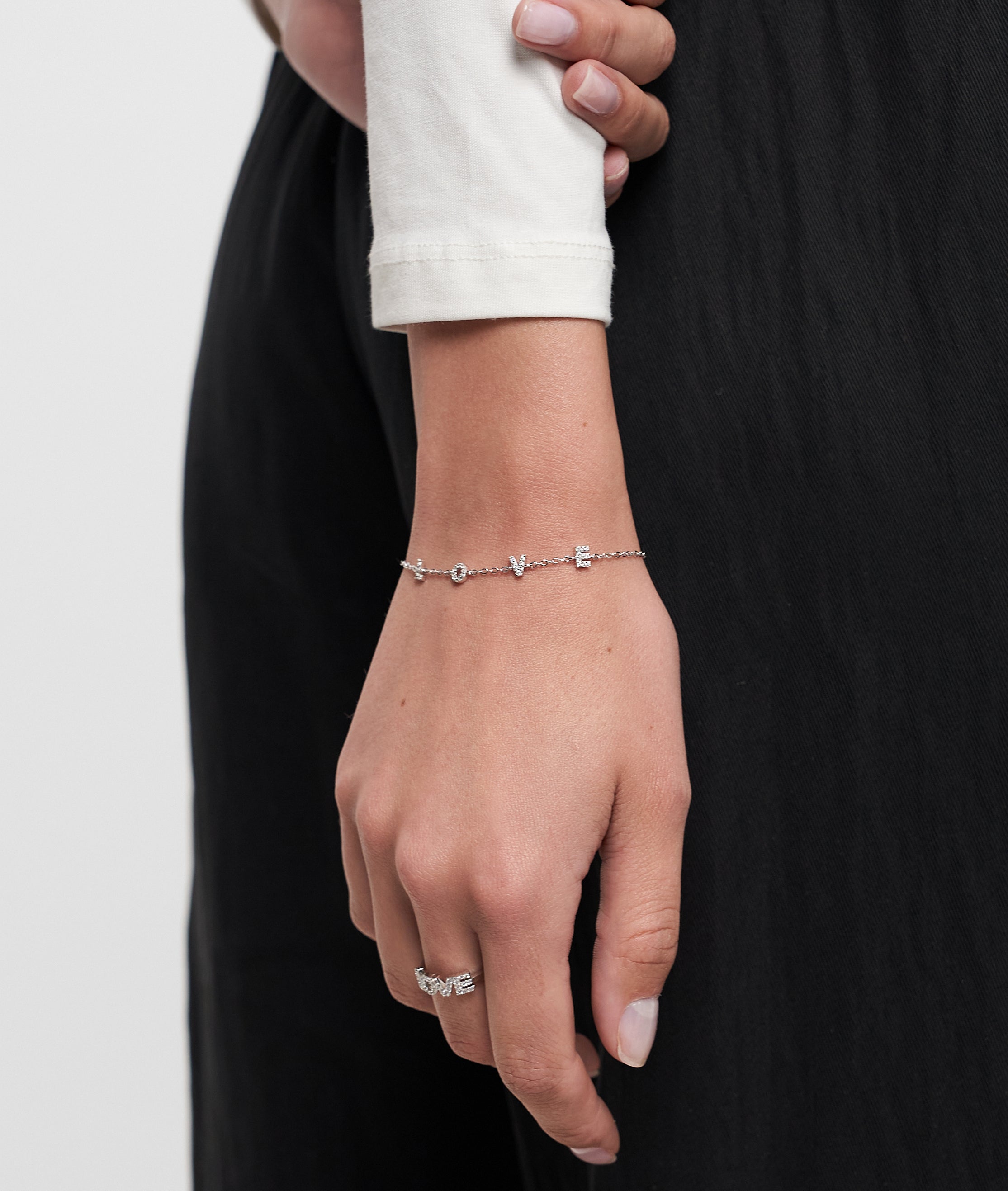 Eine Hand, die das Tamaris Armband aus der Silver Love Collection von Tamaris mit Zirkoniasteinen und einem Silberring trägt, ruht auf einer schwarzen Hose.