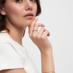 Eine Frau in einem weißen Hemd posiert mit ihrer Hand am Kinn und trägt zarten Schmuck, darunter einen LOVE Anhänger Ring und das Tamaris Silver Love Collection Armband von Tamaris.