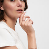 Eine Frau in einem weißen Hemd posiert mit ihrer Hand am Kinn und trägt zarten Schmuck, darunter einen LOVE Anhänger Ring und das Tamaris Silver Love Collection Armband von Tamaris.