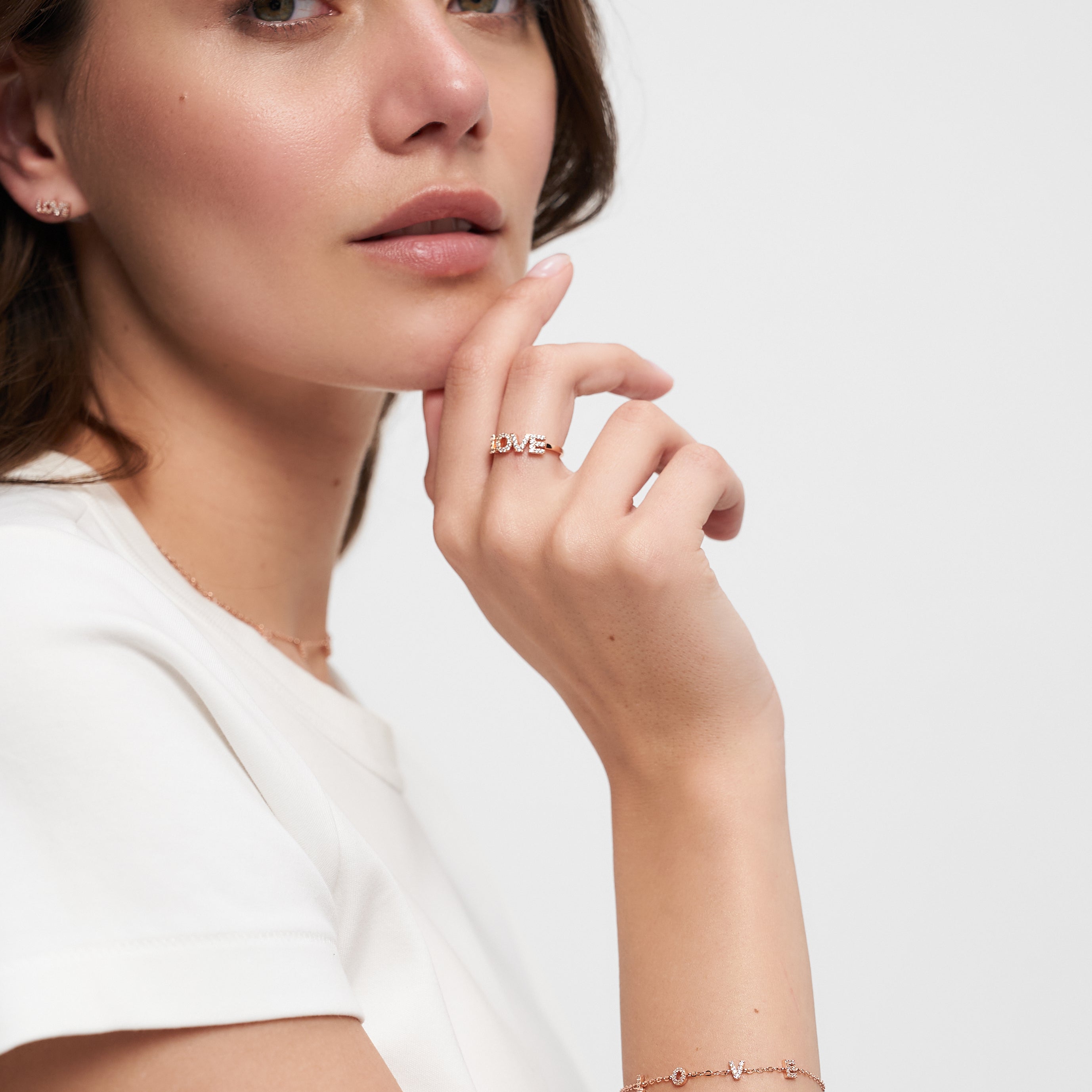 Eine Frau in einem weißen Hemd posiert mit ihrer Hand am Kinn und trägt zarten Schmuck, darunter einen LOVE Anhänger Ring und das Tamaris Silver Love Collection Armband von Tamaris.