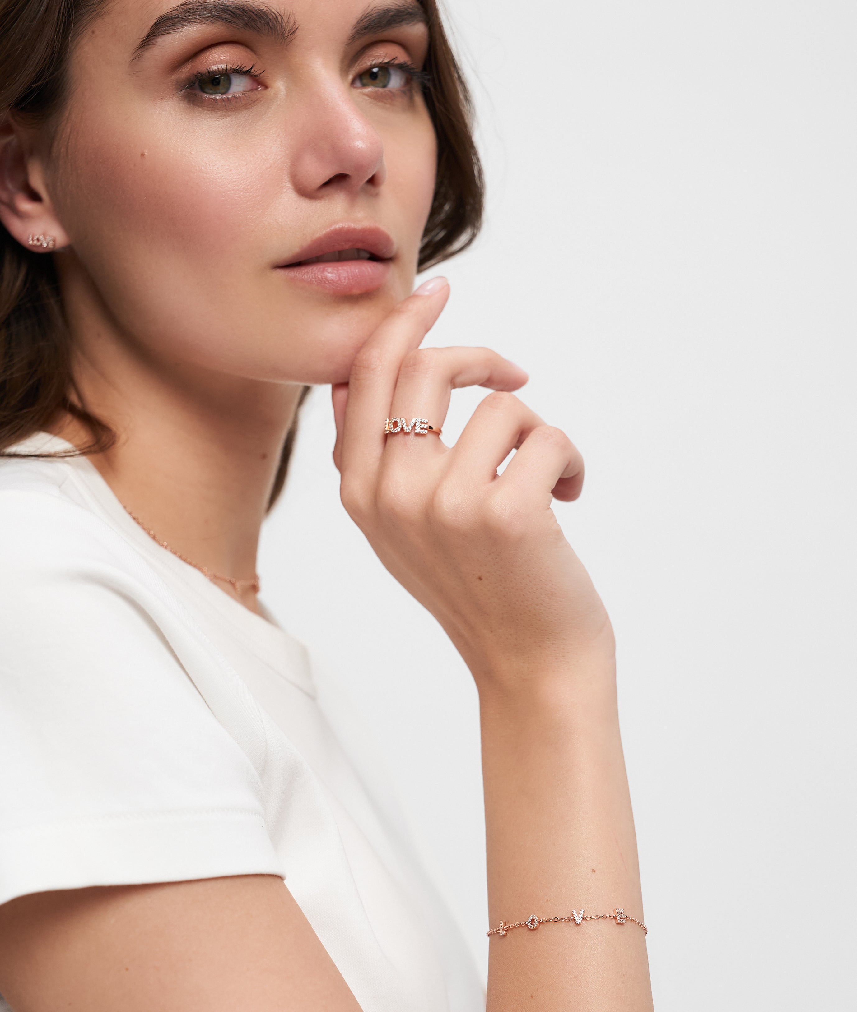 Eine Frau in einem weißen Hemd posiert mit ihrer Hand am Kinn und trägt zarten Schmuck, darunter einen LOVE Anhänger Ring und das Tamaris Silver Love Collection Armband von Tamaris.